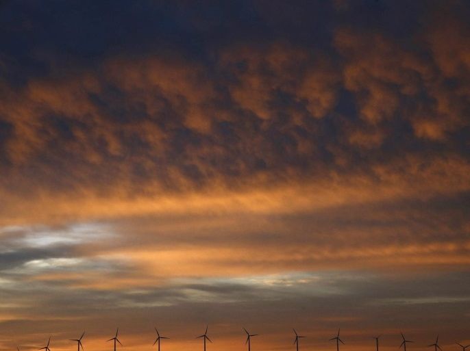 Windmills stand in line on the horizon under a dramatically illuminated cloudy sky during daybreak near Pamplona, northern Spain, early 16 October 2016 morning.