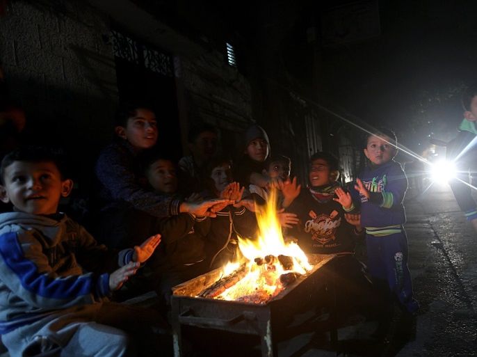 Palestinians refugees boys reacting as they warm up in front of a fire during a power outage as they endure the cold weather in Al Shateaa refugee camp, in the west of Gaza City, on 28 December 2016. Residents of Gaza, home to 1.8 million people, experience some 16 houres of electricity outage per day