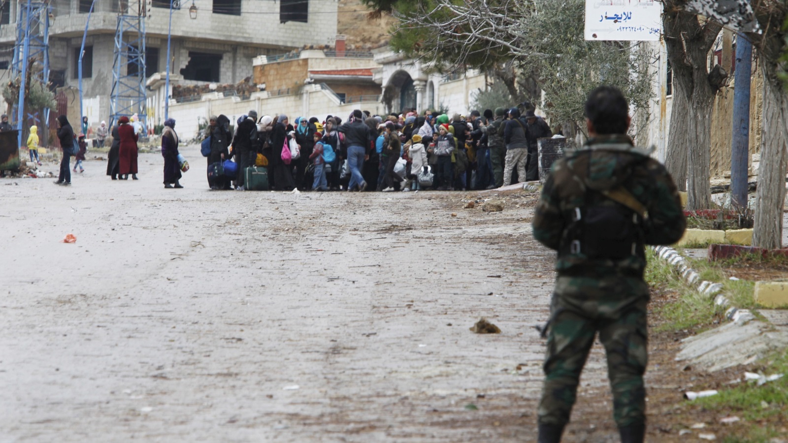 جندي من النظام السوري يراقب المغادرين من مدينة إدلب بعد حصولهم على إذن من النظام (رويترز)