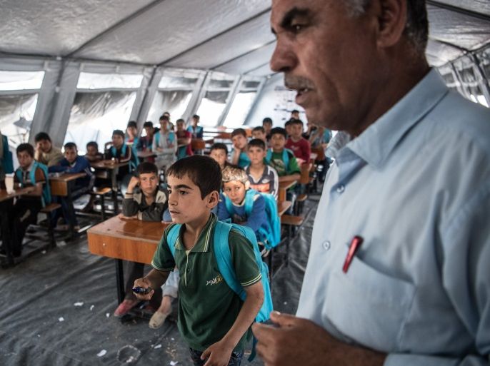 MOSUL, IRAQ - APRIL 15: A boy walks past a teacher to write on a whiteboard in class at a school in Khazir refugee camp on April 15, 2017 near Mosul, Iraq. Khazir camp, with a capacity of roughly 30,000 and along with several other camps near the city of Mosul, provides home for the approximately 300,000 people who have fled Iraq's second largest city as Iraqi government forces continue the military campaign to recapture the city from Islamic State who captured it in 2014. (Photo by Carl Court/Getty Images)