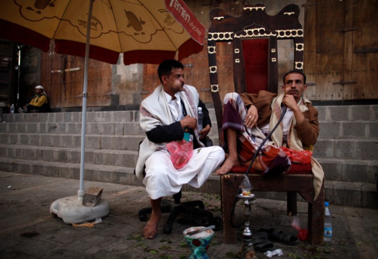 Men chew on qat, a mild stimulant, as they sit on chairs on the side of a road in the Old Sanaa city