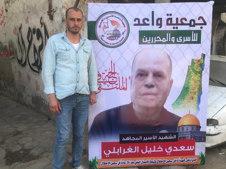 محمود الغرابلي يقف إلى جوار لافتة كبيرة لصورة والده في بيت العزاء بمدينة غزة-رائد موسى-الجزيرة نت