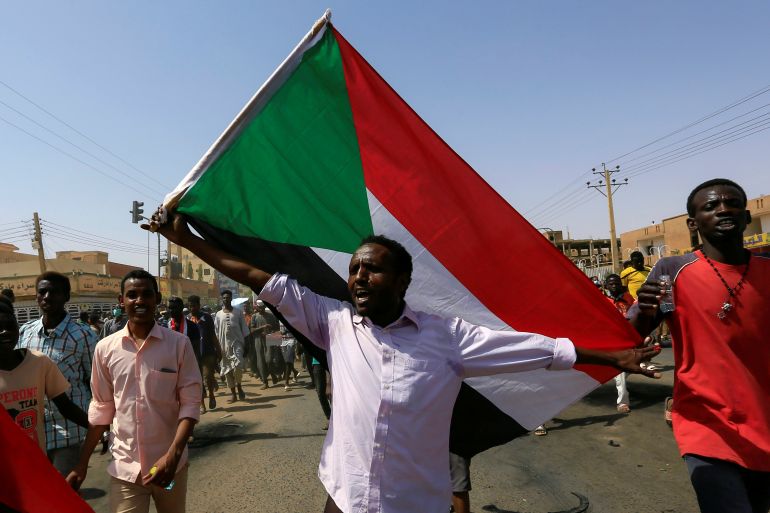 A civilian holds the national flag as members of Sudanese pro-democracy protest on the anniversary of a major anti-military protest, as groups loyal to toppled leader Omar al-Bashir plan rival demonstrations in Khartoum
