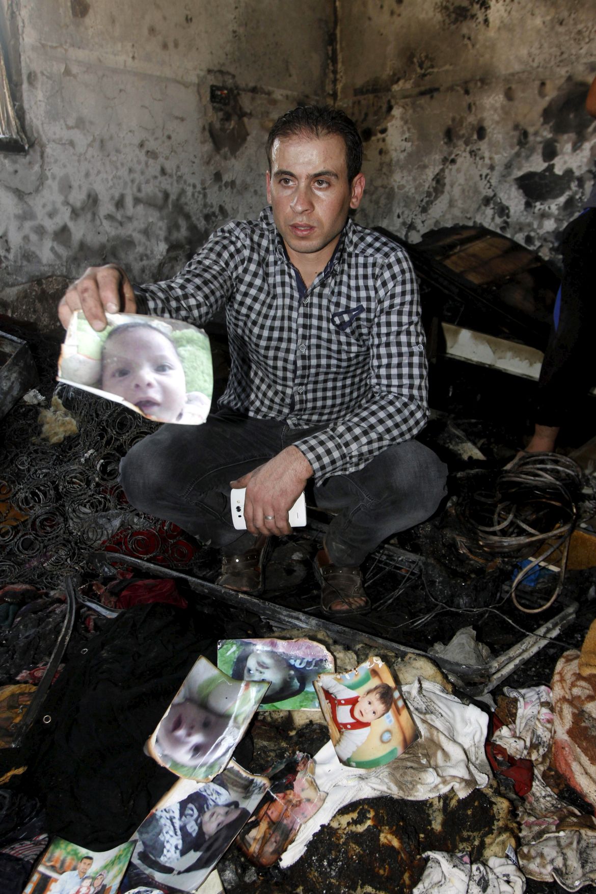 A relative shows a picture of Palestinian baby Ali Dawabsheh, who was killed after his family's house was set on fire in a suspected attack by Jewish extremists, at the burnt house in Duma village near the West Bank city of Nablus