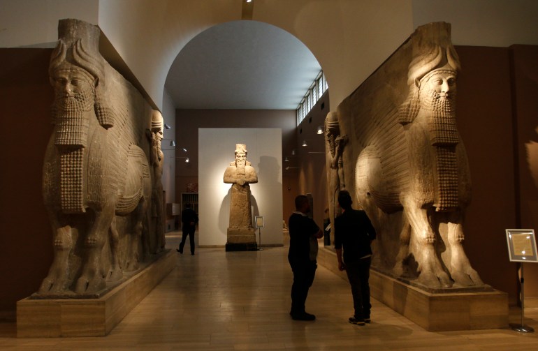 People look at ancient Assyrian human-headed winged bull statues at the Iraqi National Museum in Baghdad