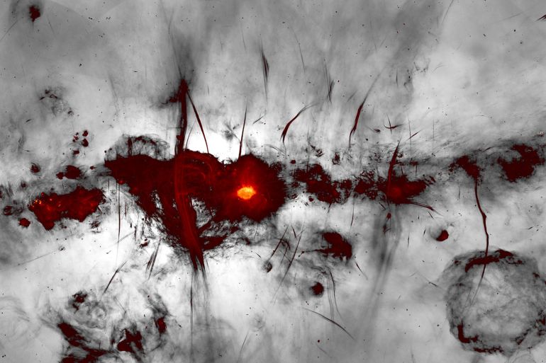 The new MeerKAT image of the Galactic centre region is shown with the Galactic plane running horizontally across the image. Many new and previously-known radio features are evident, including supernova remnants, compact star-forming regions, and the large population of mysterious radio filaments. The broad feature running vertically through the image is the inner part of the (previously discovered) radio bubbles, spanning 1400 light-years across the centre of the Galaxy. Colours indicate bright radio emission, while fainter emission is shown in greyscale. Credit: I. Heywood, SARAO.