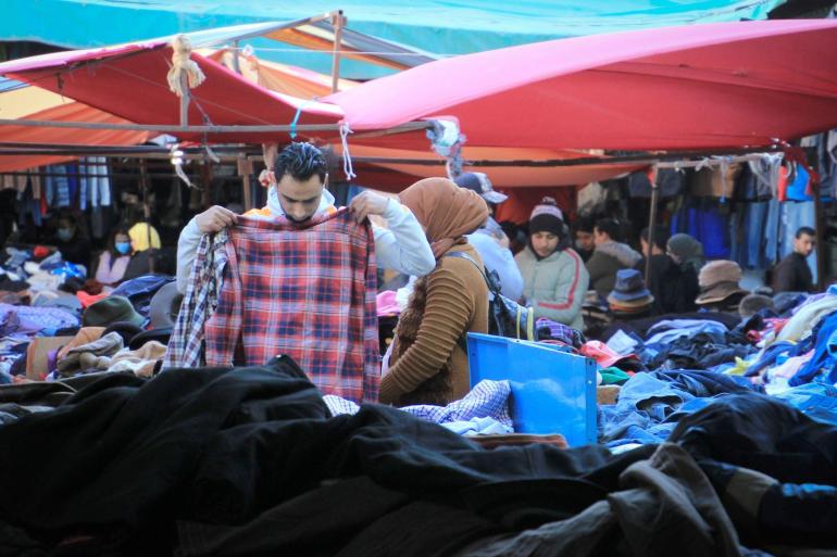 © DPA (Arabic) رجل يمسك بقميص في سوق لبيع الملابس المستعملة. Cindy Riechau/dpa