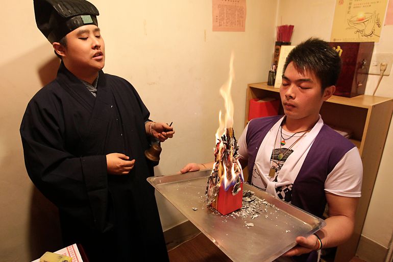 Lu Wei-ming, priest of the Wei-ming temple, and a worshipper burn a Taoist paper amulet during a prayer ritual at the temple in New Taipei city