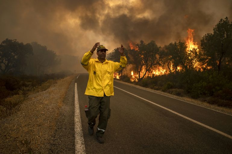 A forest ranger reacts as a forest fire rages in the background near Ksar el-Kebir in the Larache region, on July 15, 2022. (Photo by FADEL SENNA / AFP)