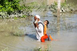 A man wades through flood waters carrying his grand daughter on his back following rains and floods during the monsoon season in Charsadda, Pakistan August 28, 2022. REUTERS/Fayaz AzizAziz