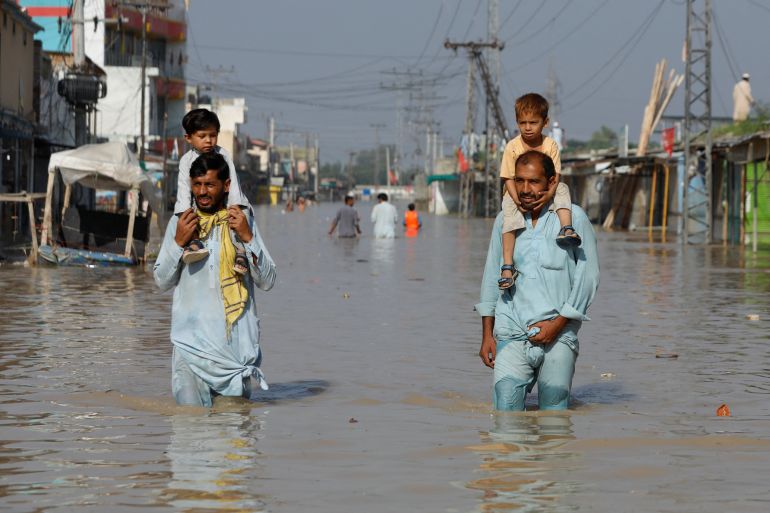 Men carry children on their shoulders and wade along a flooded road, following rains and floods during the monsoon season in Nowshera