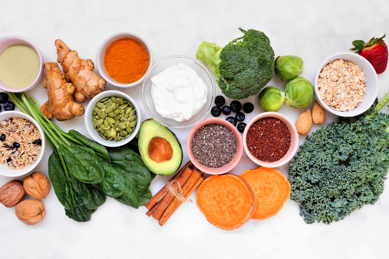 Healthy food ingredients. Above view table scene on a white marble background. Super food concept with green vegetables, berries, whole grains, seeds, spices and nutritious items.