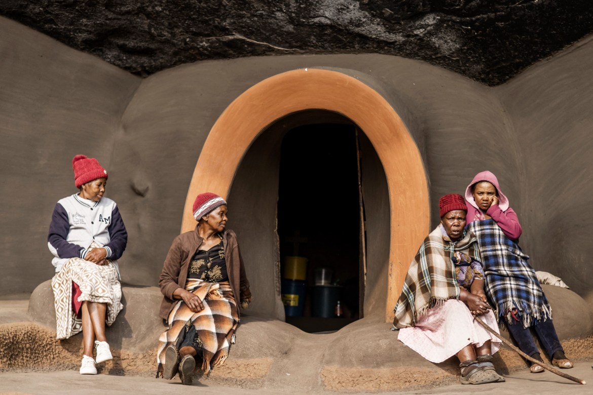 Makoenweo, left, 60, and Mamtsaseng Khutsoane, second from left, 66, residents of the Kome Caves, sit with other women in front of dwellings. [Marco Longari/AFP]