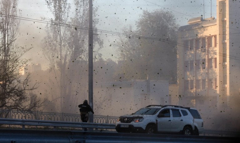 A police officer watches stones and other debris flying through the air as Russian kamikaze drones hit the centre of the capital Kyiv. [Vadym Sarakhan/AP Photo