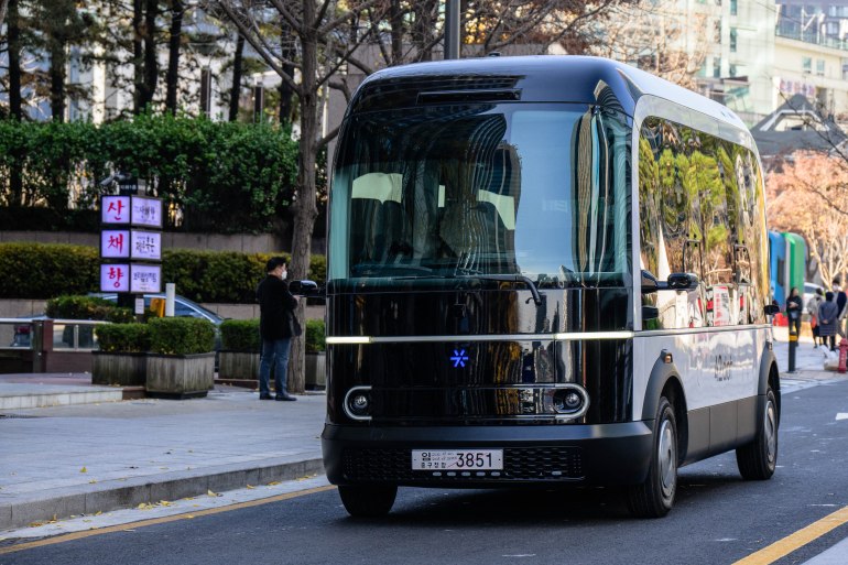 This photo taken in Seoul on November 23, 2022 shows a bus with a blue coloured logo (front C) which indicates that autonomous driving is taking place, as it approaches a stop on the country's first self-driving bus route run by 42 Dot, a start-up owned by South Korea's Hyundai which created the automomous driving technology. - South Korea's capital launched its first self-driving bus route on November 25, part of an experiment which engineers said aims to make the public feel more comfortable with driverless vehicles on the roads. (Photo by Anthony WALLACE / AFP)