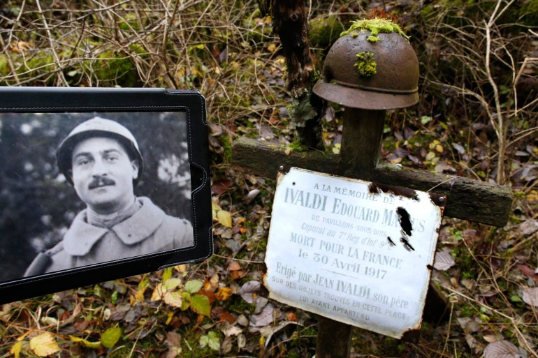 A portrait of French WWI soldier Edouard Marius Ivaldi is displayed on a tablet, in this illustration picture, alongside his battlefield grave memorial, a wooden cross with a battlefield helmet in Champagne, eastern France, November 3, 2015. The plaque which reads in part, "In Memory of Edouard Marius Ivaldi, Corporal in the 7th Infantry Regiment. Died for France on April 30, 1917", was placed there by Ivaldi's father in 1919. World War One historians estimate that on the western front half of the fallen soldiers were never found or identified. Edouard Marius Ivaldi is one of these. After the war, his father Jean-Joseph searched for the remains of his son and started the grieving process. In 1919 he placed a wood cross on the spot where his son fell in combat, then in 1924 he placed a plaque with his son's name in the chapel of the Navarin Ossuary. Almost 100 years later, this place of private memory, its location unknown to visitors, has remained untouched over time. Picture taken November 3, 2015. REUTERS/Charles Platiau TPX IMAGES OF THE DAY