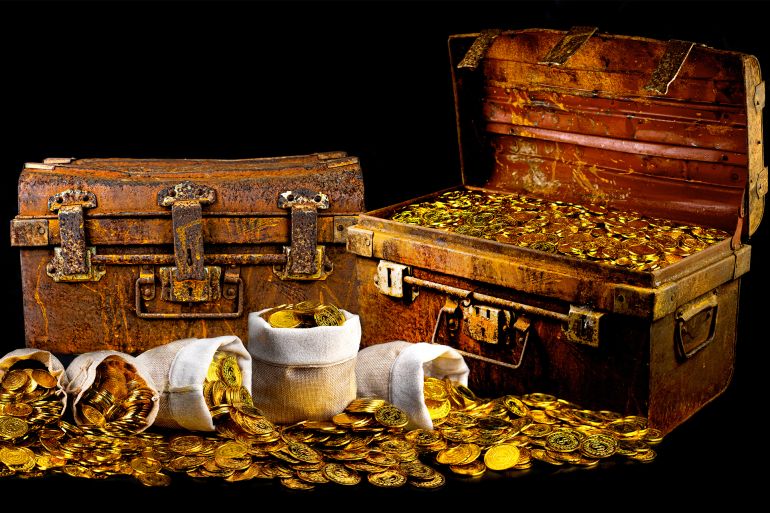 Stacking lots of gold coins in treasure chest old on black background GettyImages-1330372165