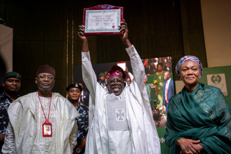 President-Elect Bola Tinubu, center, displays his certificate, accompanied by his wife Oluremi Tinubu, right, and chairman of the Independent National Electoral Commission (INEC) Mahmood Yakubu, left, at a ceremony in Abuja, Nigeria Wednesday, March 1, 2023. Election officials declared Tinubu the winner of Nigeria's presidential election Wednesday, keeping the ruling party in power in Africa's most populous nation. (AP Photo/Ben Curtis)