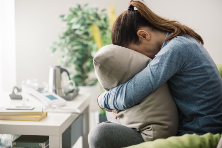 Unhappy lonely depressed woman at home, she is sitting on the couch and hiding her face on a pillow, depression concept; Shutterstock ID 504503110; purchase_order:aj midan; job:; client:; other: