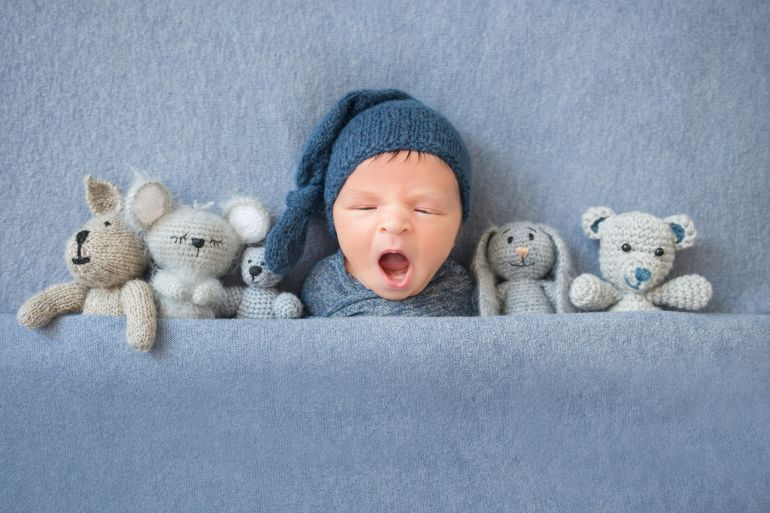 shutterstock_1056232421 Newborn baby boy yawning and lying between plush toys
