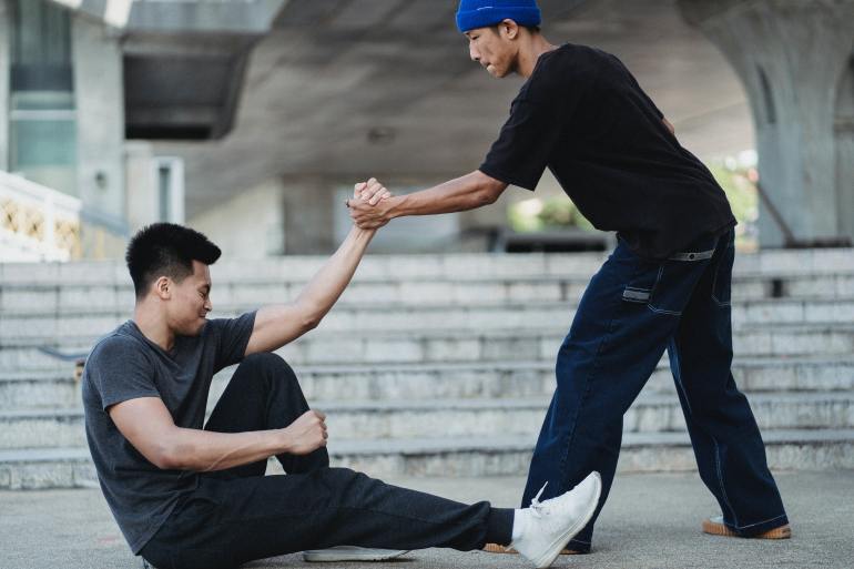 Asian man helping friend to get up from ground