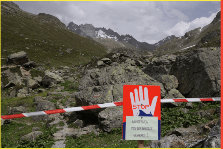 GALTUR, AUSTRIA - JUNE 22: A sign warns that local authorities have closed the hiking trail as partially collapsed Fluchthorn mountain (grey peak) stands in the distance on June 22, 2023 near Galtur, Austria. On June 12 approximately one million cubic meters of rock fell from the mountain into the valley below, causing no injuries but shortening the mountain by 19 meters, from 3,399 meters to 3,380 meters, and bringing down the cross on its peak. Scientists blame melting permafrost, which is undoing the natural bonding effect of ice within high alpine rock. Average temperatures have risen twice as fast in the European Alps compared to lowlands over recent decades. (Photo by Sean Gallup/Getty Images)