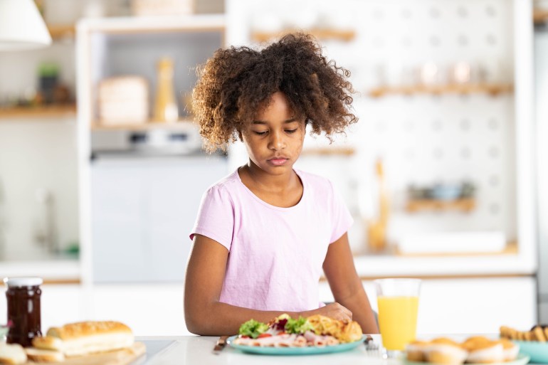 Displeased African American girl unwilling to eat her breakfast in dining room.