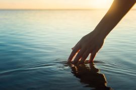 A female hand touching the ocean water in front of a beautful sunset during summer time.