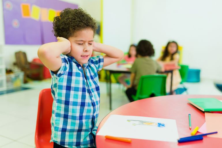 Overwhelmed preschooler with autism in kindergarten - stock photo Upset autistic little boy covering his ears and feeling distressed and overwhelmed by the loud noises in preschool