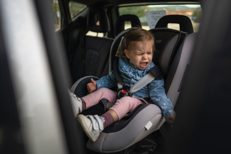 One girl small caucasian toddler female child sitting in the safety car seat chair 18 months old cry protest negative emotion transportation concept copy space