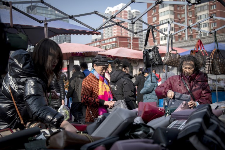 People look at handbags to sell at a market in Beijing on February 27, 2019. (Photo by Nicolas ASFOURI / AFP)
