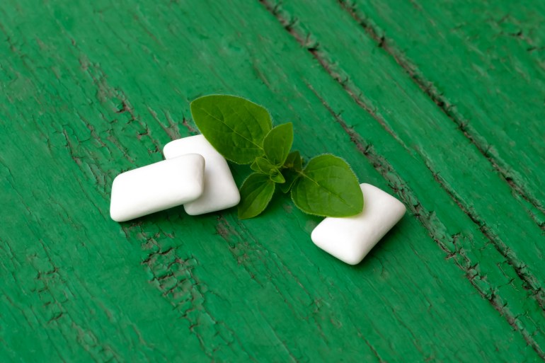 Group of white cubes of mint chewing gums with fresh peppermint leaves on bright green wooden background. Chewing gum pieces