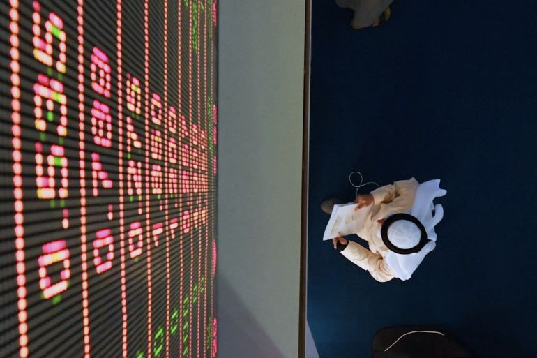 A trader stands below a big screen at the Dubai Financial Market in the Gulf emirate on January 6, 2020, as Gulf bourses were hit by a panicky sell-off amid Iranian vows of retaliation over the US killing of a top general. All seven bourses in the Gulf Cooperation Council (GCC) states closed in the red, on the first trading day since the death of powerful military commander Qasem Soleimani. (Photo by Karim SAHIB / AFP)