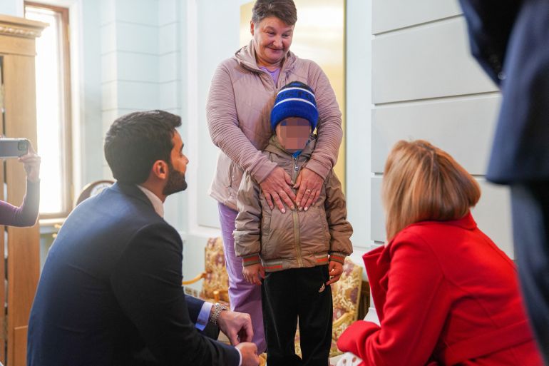 A 7-year-old Ukrainian boy, who is the first child released under a new mechanism Qatar has set up with the goal of repatriating children from Russia to Ukraine, stands with his grandmother while interacting with Russia's Commissioner for Children's Rights, Maria Lvova-Belova and a Qatari diplomat in this handout image taken at Qatar's embassy in Moscow, Russia October 13, 2023. Qatar's Ministry of Foreign Affairs/Handout via REUTERS THIS IMAGE HAS BEEN SUPPLIED BY A THIRD PARTY. MANDATORY CREDIT. NO RESALES. NO ARCHIVES. IMAGE HAS BEEN BLURRED AT SOURCE.