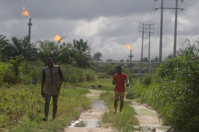 Two men walk past gas flares belonging to the Agip Oil company in Idu, Niger Delta area of Nigeria, Friday, Oct. 8, 2021. (AP Photo/Sunday Alamba)