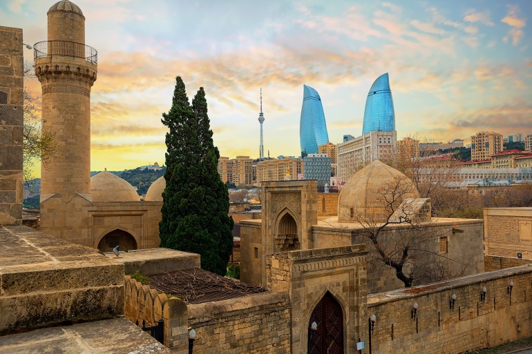 Baku city, Azerbaijan, view of the historical mosques and the walls of Shirvanshahs palace in the Old town and modern glass Flower Towers skyscrapers in dramatic sunset light