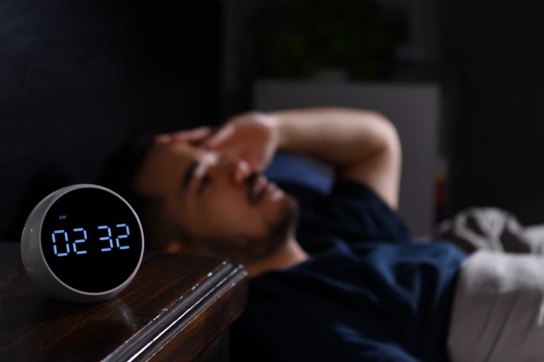 Depressed young Asian man lying in bed cannot sleep from insomnia. focus on clock