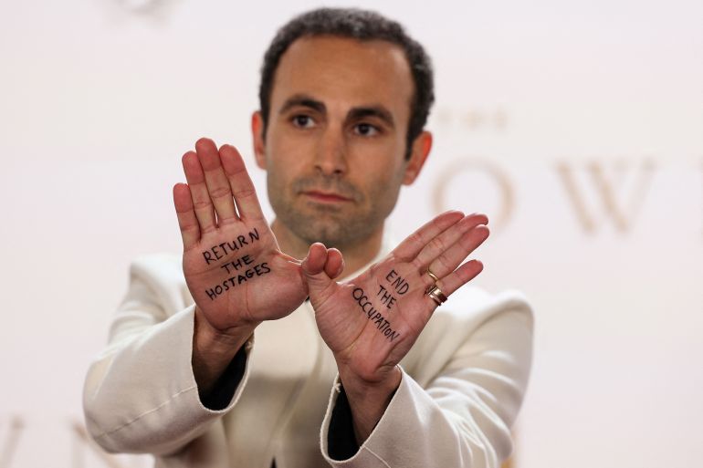British actor Khalid Abdalla holds up his hands with two messages reading "Return the hostages" (L) and "End the occupation" as he poses on the red carpet upon arrival to attend the Premiere of "The Crown Finale Celebration" at the Royal Festival Hall, in London, on December 5, 2023. (Photo by Adrian DENNIS / AFP)