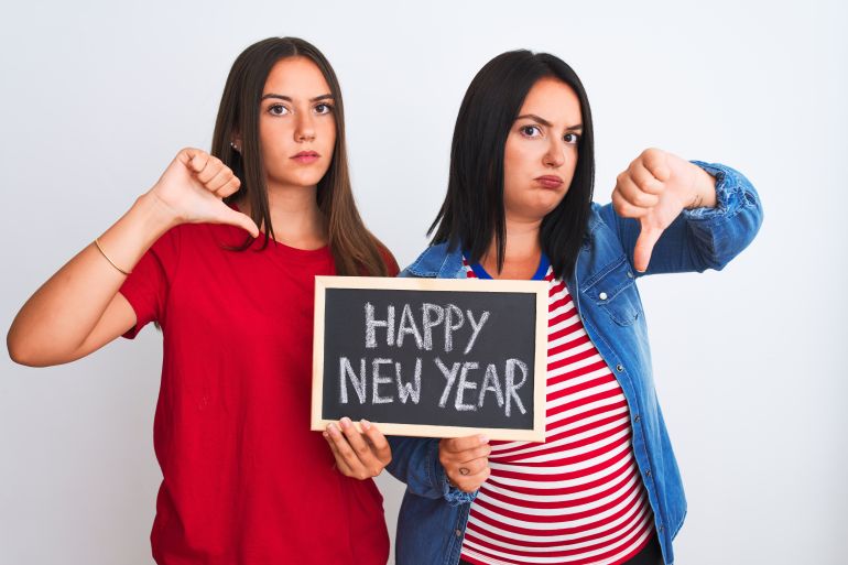 Beautiful women holding blackboard happy new year message over isolated white background with angry face, negative sign showing dislike with thumbs down, rejection concept