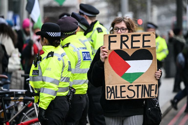 A pro-Palestinian supporter holds a placards as she walks past Met police officers while taking part in a "Day of Action for Palestine" demonstration outside the British multinational arms, security and aerospace company BAE Systems, in London, on January 20, 2024. - Hamas's unprecedented attack on Israel on October 7, 2023 which left about 1,140 dead in Israel, mostly civilians, according to an AFP tally based on official figures, and saw 250 hostages dragged back into Gaza sparked the war which is still raging in the besieged Gaza Strip. After almost 100 days of war, at least 23,357 people have been killed in the fighting in Gaza, the majority of them women and children, according to the Hamas health ministry -- or almost one percent of the population. (Photo by JUSTIN TALLIS / AFP)