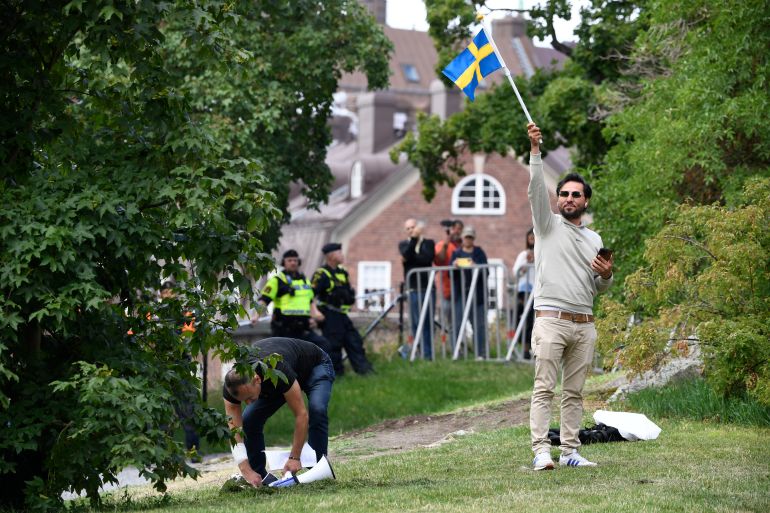 epa10757833 Protestor Salwan Momika (R) waves a Swedish flag while a police officer pick sup papers next to him during his demonstration outside the Iraqi embassy in Stockholm, Sweden, 20 July 2023, where he announced he would burn a copy of the Koran and an Iraqi flag. This follows previous demonstrations against Sweden around the world for allowing planned protests where the Koran was to be burned. EPA-EFE/Oscar Olsson SWEDEN OUT