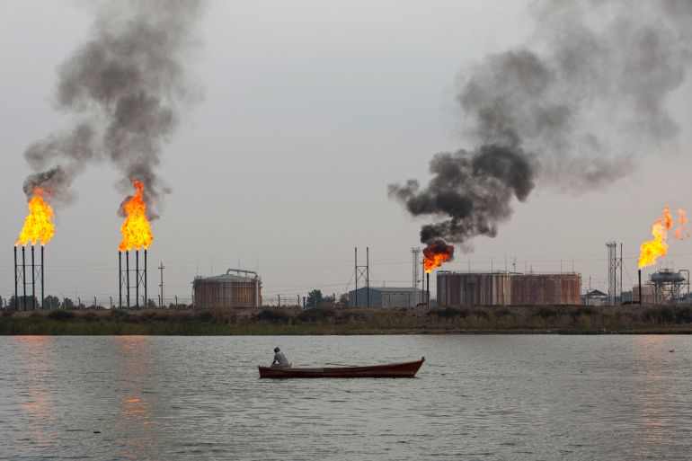 A boat sails past the Umm Qasr port near Iraq's southern port city of Basra on February 11, 2022. In the oilfields of southern Iraq, billions of cubic feet of gas literally go up in smoke, burnt off on flare stacks for want of the infrastructure to capture and process it. The flares produce vast amounts of carbon dioxide and other greenhouse gases, contributing to global warming without any economic or social benefit. (Photo by Hussein FALEH / AFP)