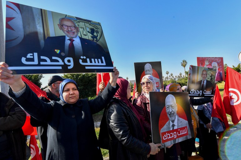 Supporters of the head of Tunisia's Islamist movement Ennahdha Rached Ghannouchi (placards) express their support as he arrives to a police station in Tunis ,on February 21, 2023, in compliance to the summons of an investigating judge. (Photo by FETHI BELAID / AFP)