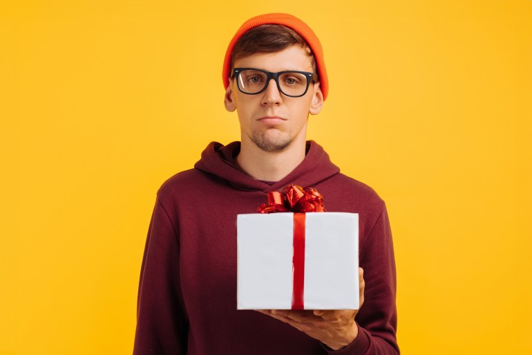 unhappy young guy in an orange hat with glasses and a red sweater is unhappy with his gift, festive mood, new year gifts