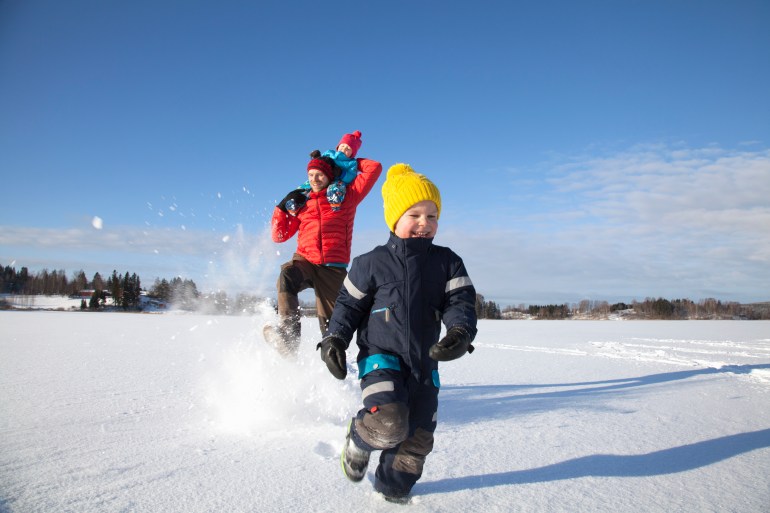 Father and two sons fooling around, running through snow covered landscape