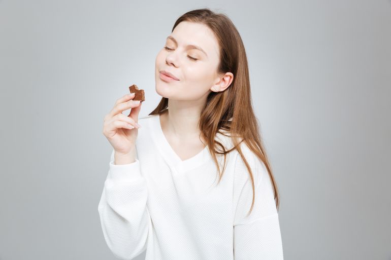 Lovely smiling teenage girl with eyes closed eating chocolate