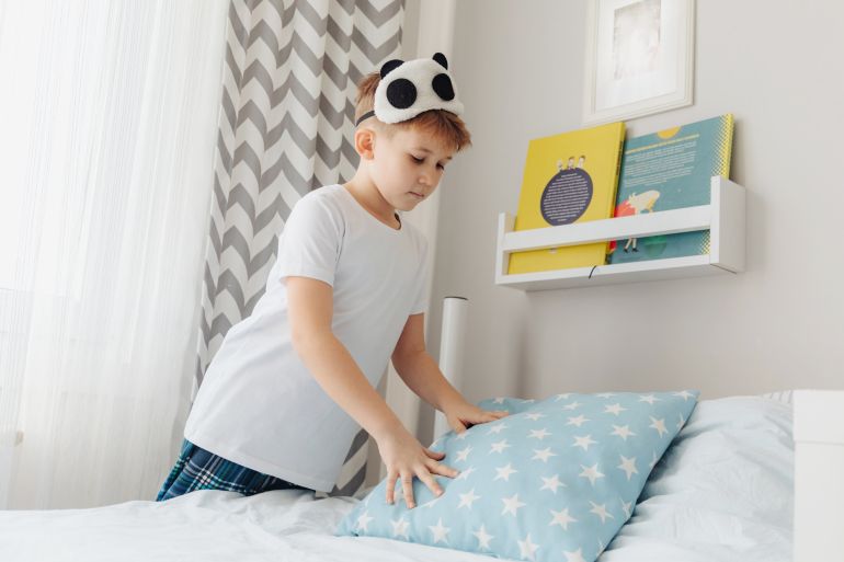 Young boy making his bed in the morning in sunny bedroom.; Shutterstock ID 2123919905; purchase_order: aljazeera ; job: ; client: ; other: