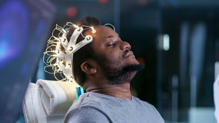 In Laboratory Man Wearing Brainwave Scanning Headset Sits in a Chair with Closed Eyes. Monitors Show EEG Reading and Graphical Brain Model. In the Modern Brain Study/ Neurological Research Laboratory.