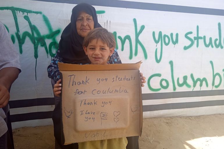 نازحة تحتضن طفلاً في رفح يحمل لافتة شكر لطلبة جامعة كولومبيا الامريكية-رائد موسى-رفح-الجزيرة نت